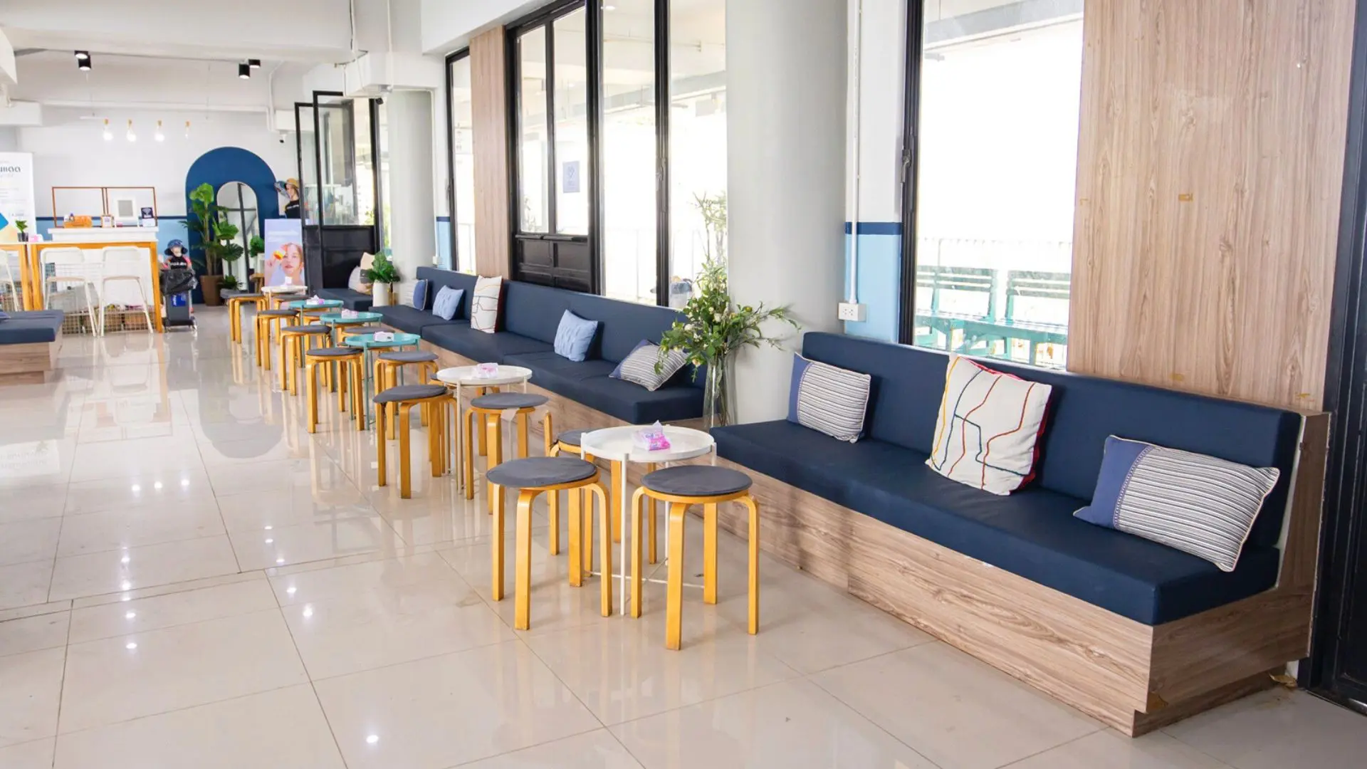Sala de espera com um banco corrido azul-marinho, almofadas, bancos de madeira e balcão de receção ao fundo