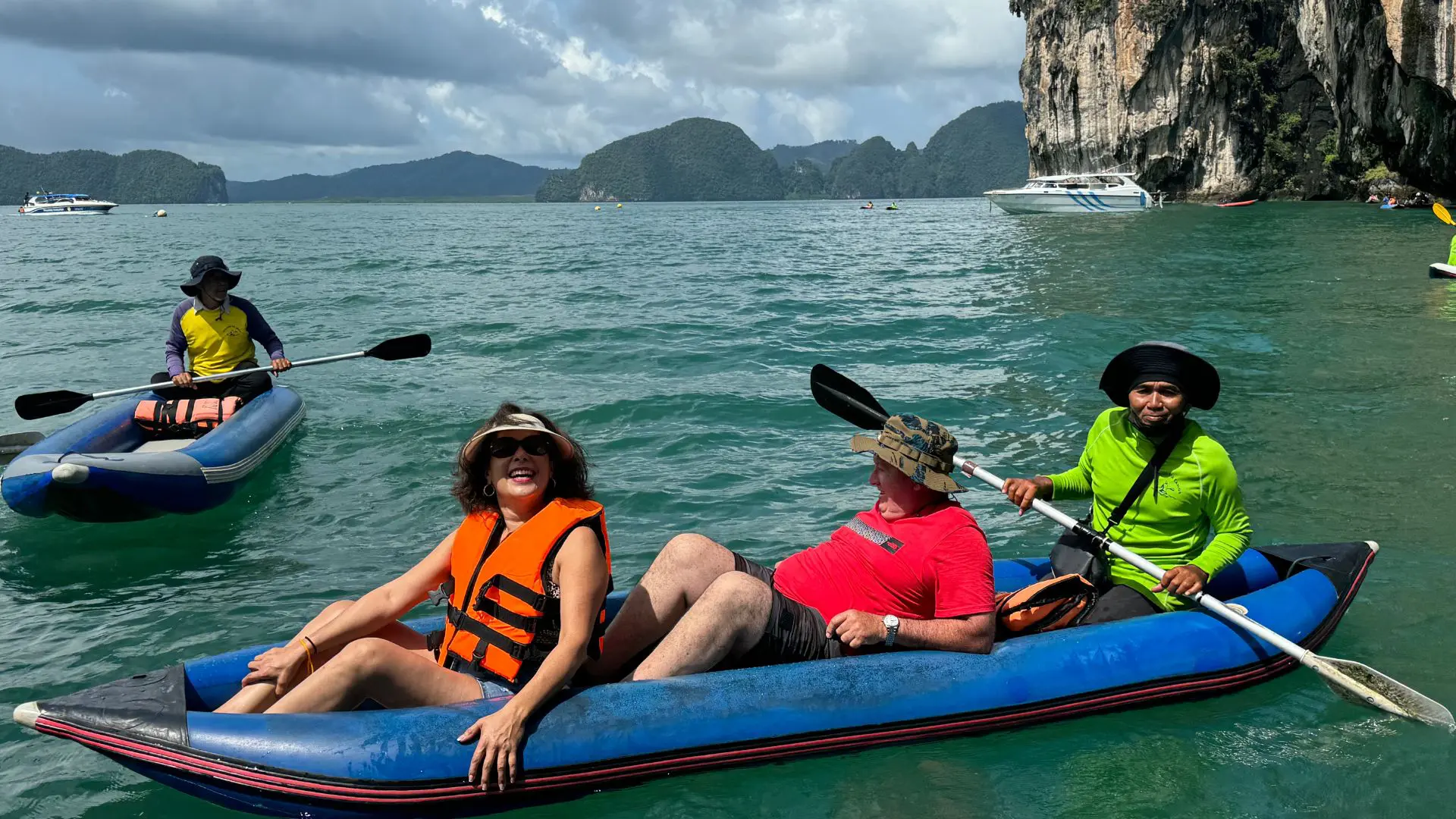 Mujer con chaleco naranja y hombre de rojo en una canoa azul que rema un guía; al fondo, otra canoa y un islote calizo