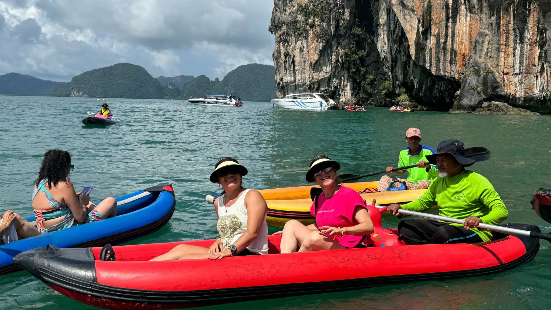 Dos mujeres, de blanco y de rosa, sonríen en una canoa roja con su guía de verde, bajo un gran acantilado de roca caliza