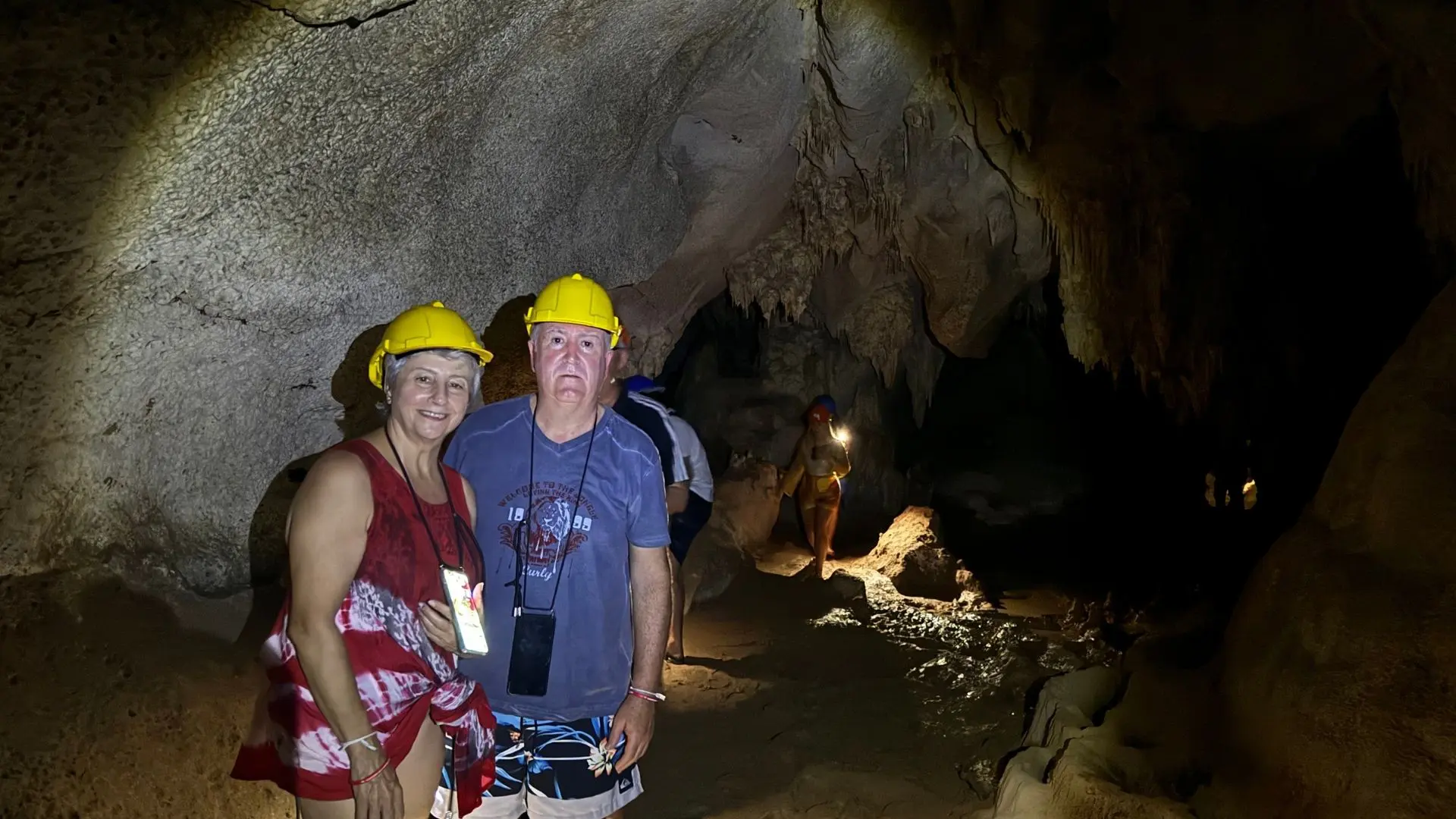 Pareja con cascos amarillos dentro de una cueva con estalactitas, seguida por otros visitantes con linterna