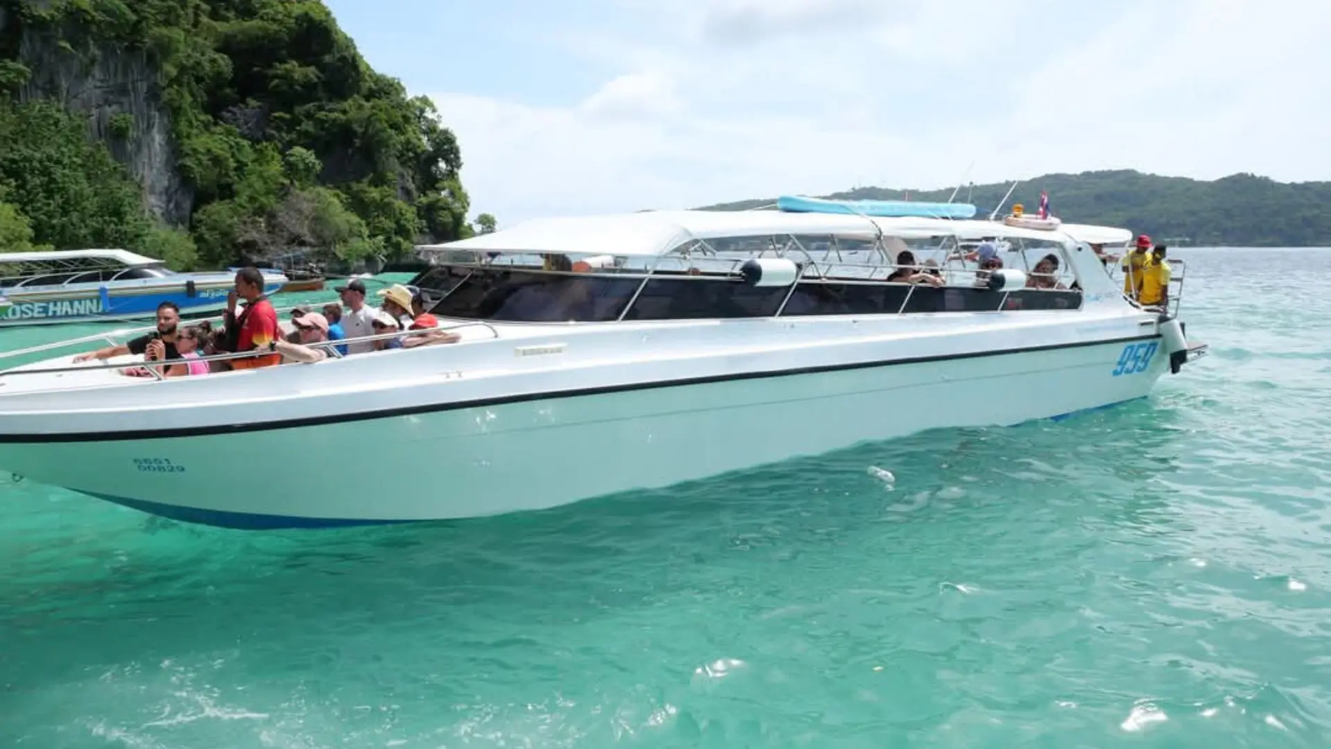 Lancha rápida blanca con el número 959 y pasajeros a bordo, sobre agua turquesa junto a un islote con vegetación