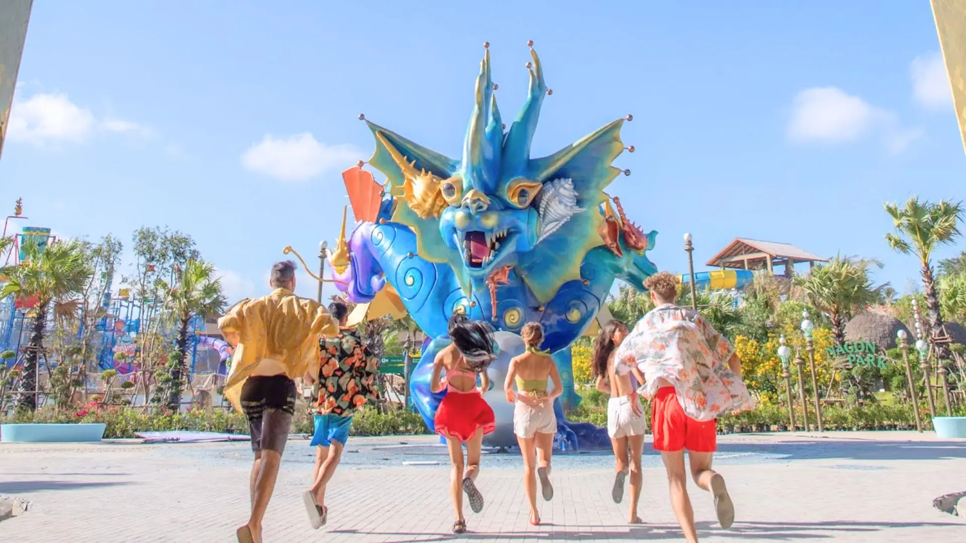 Seis jovens correm pela esplanada em direção à escultura do dragão azul, com os escorregas ao fundo