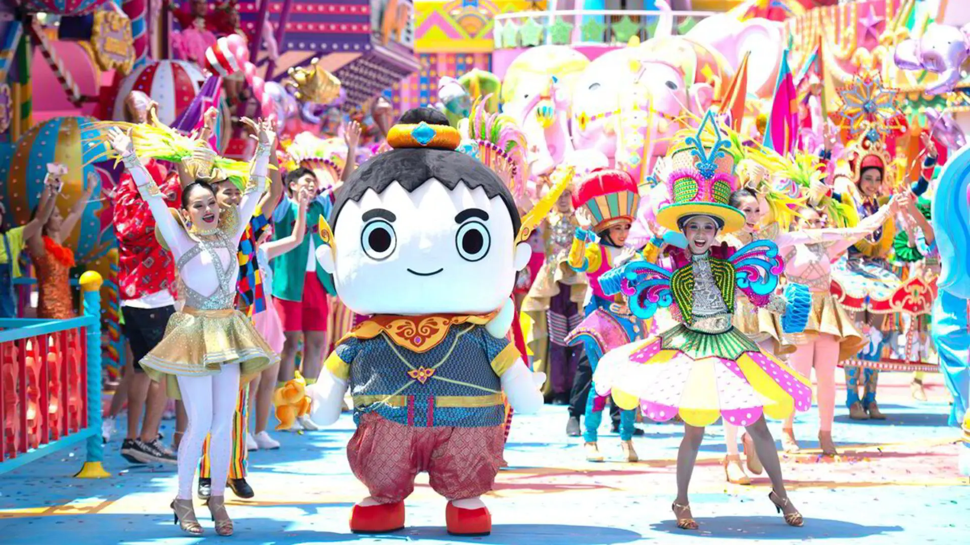 Giant round-headed mascot dressed in Thai style moves through the parade surrounded by dancers