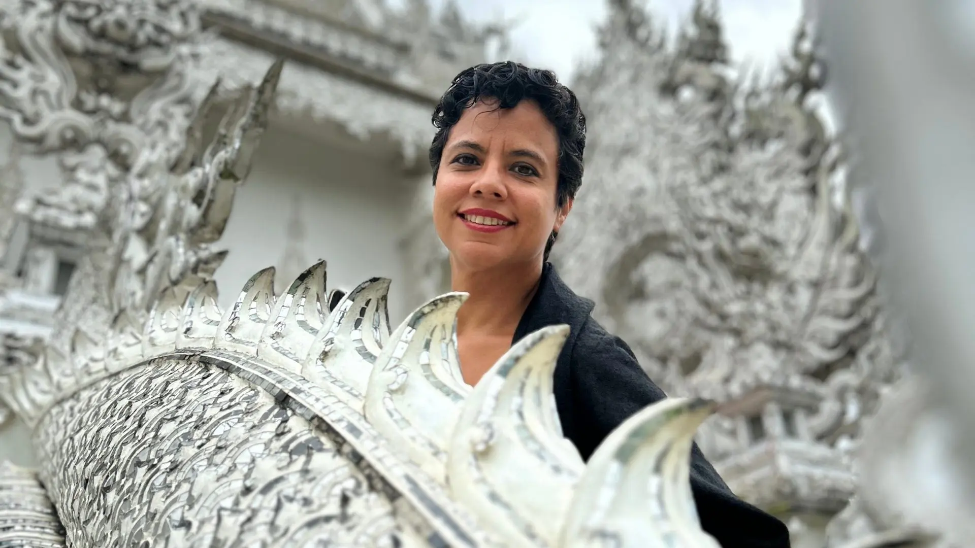 A female traveler smiles behind the mirrored crest of a white naga at the White Temple