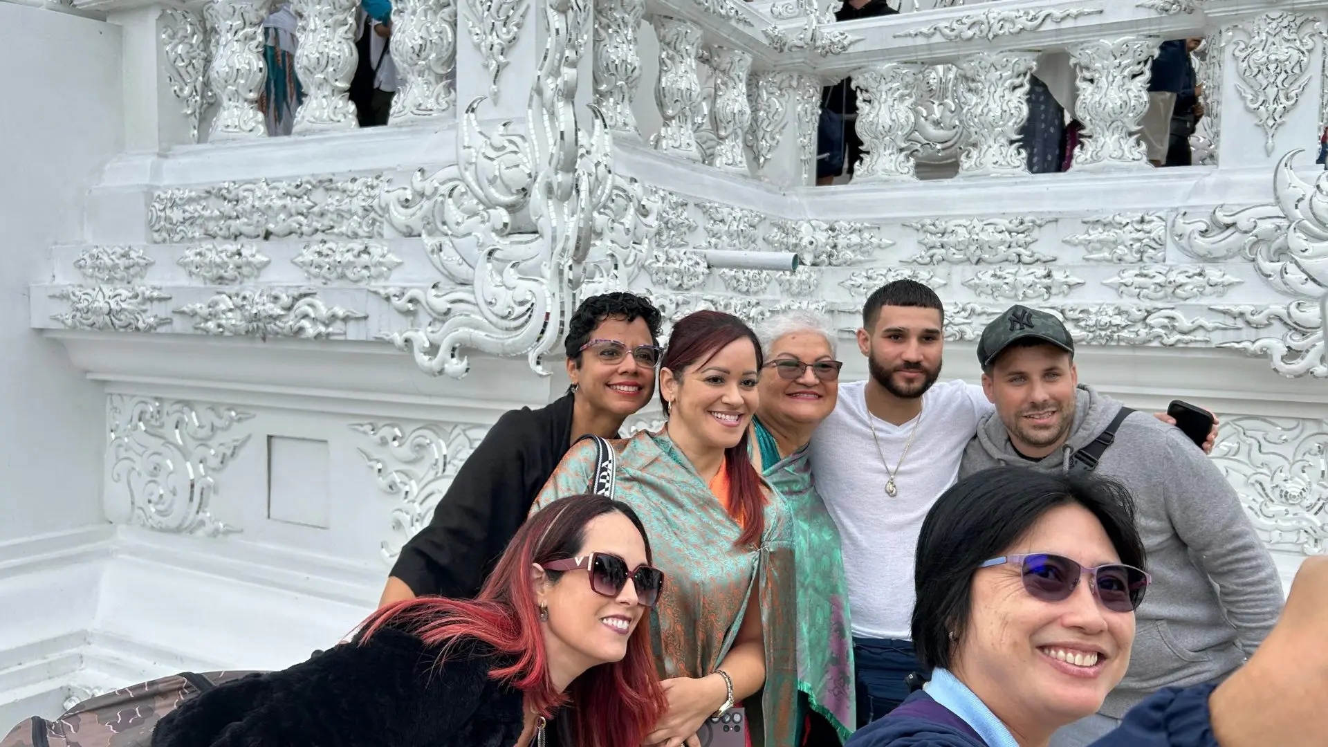 Seven travelers take a selfie in front of the carved white walls of a temple