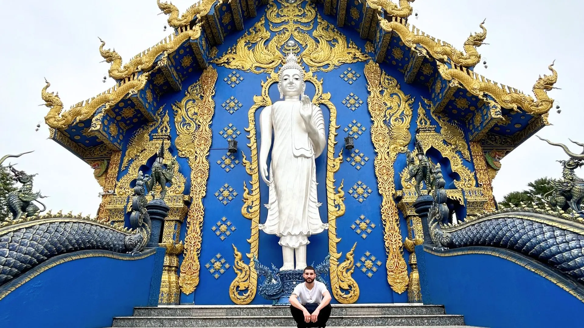 Young man crouching on the stairway of the Blue Temple, Wat Rong Suea Ten, below the large white standing Buddha