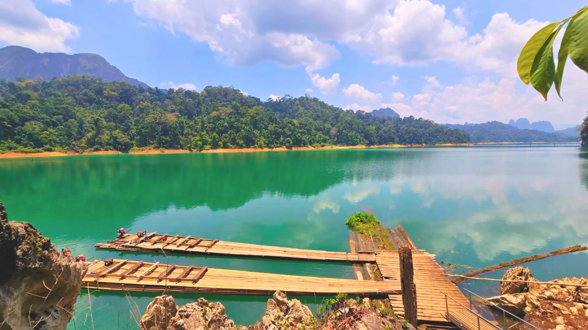 Balsas de bambú amarradas a un embarcadero de madera en Cheow Lan Lake, con la orilla de selva y montañas al fondo