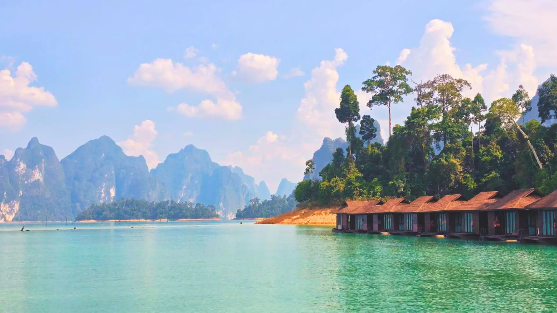 Cabañas flotantes de tejado rojizo en la orilla de Cheow Lan Lake, frente a picos de piedra caliza