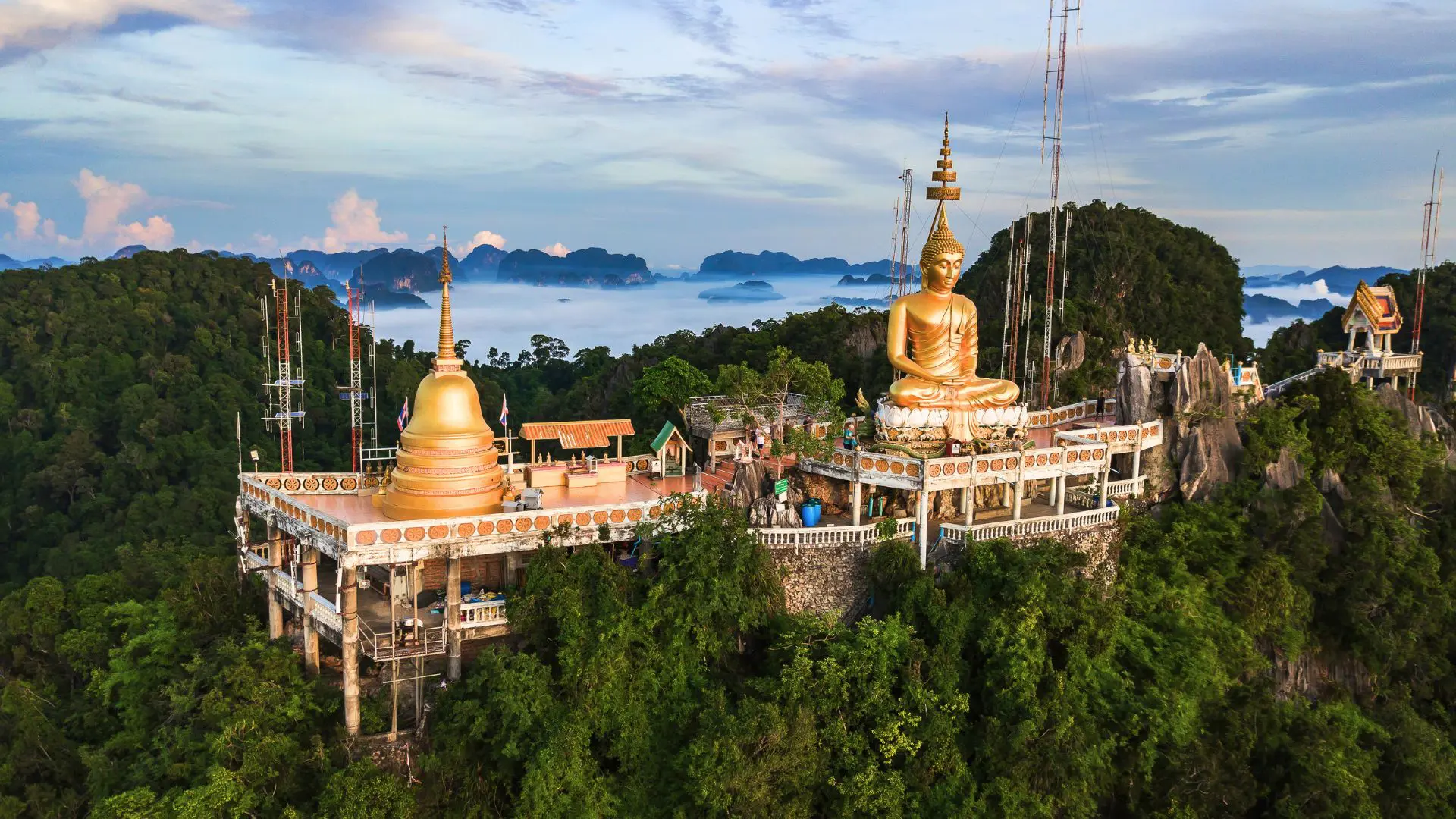 Vista aérea ao amanhecer do templo no cume: Buda dourado, pagode e montanhas rochosas entre o nevoeiro