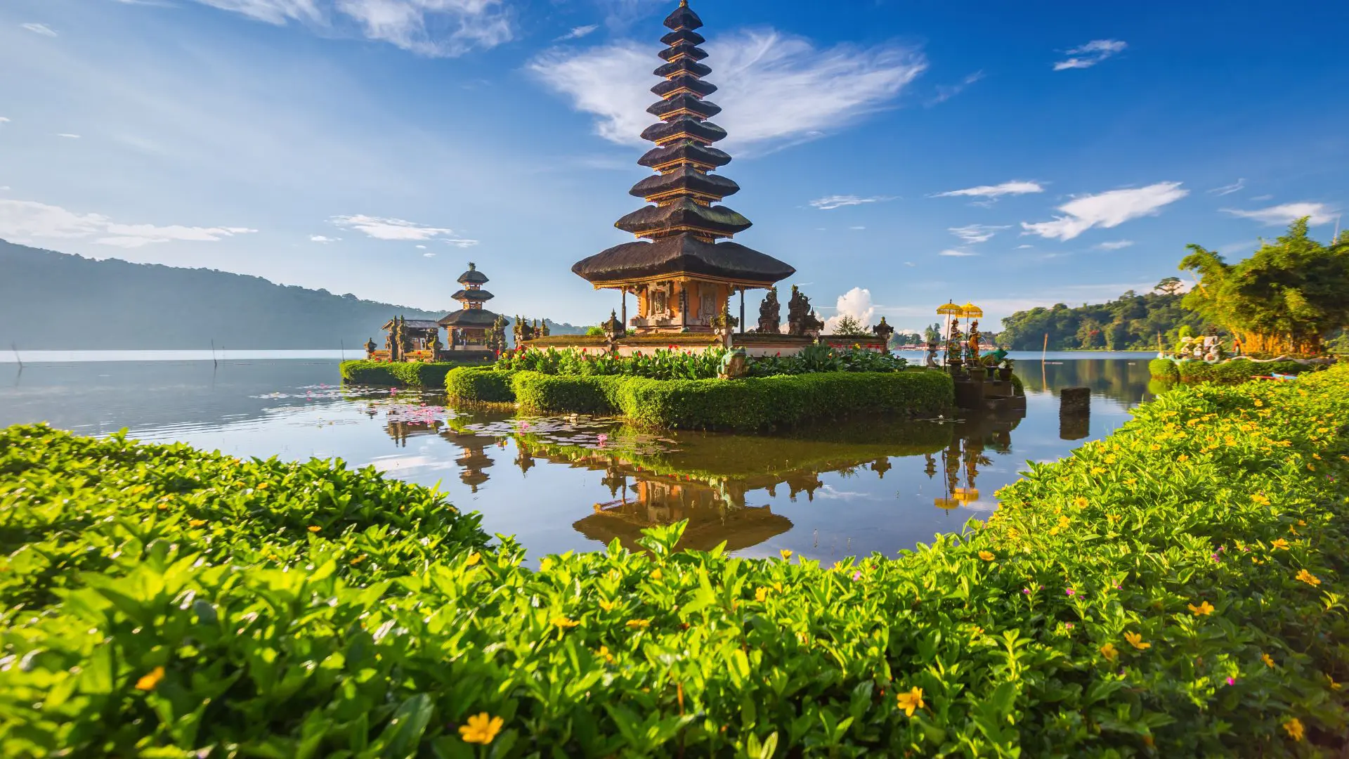 Templo balinês de telhados escalonados sobre o lago Beratan, refletido na água entre sebes verdes em flor