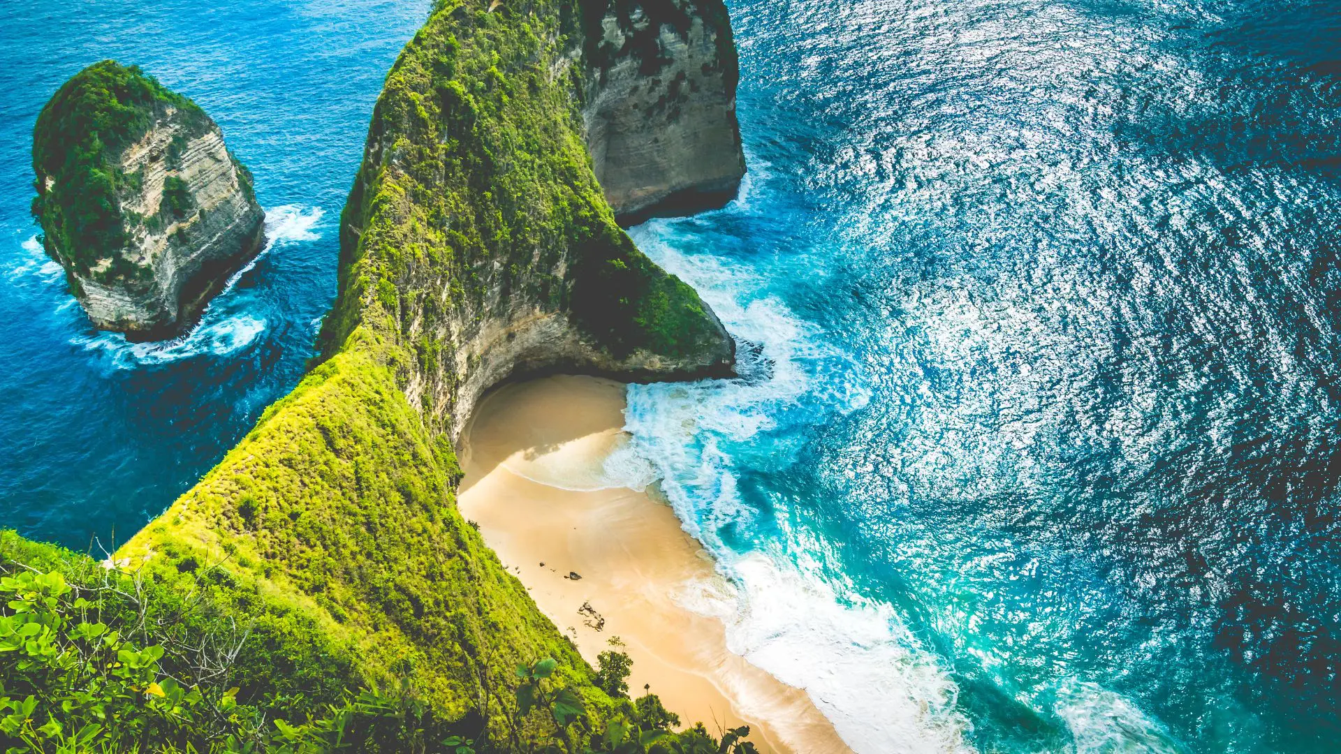 Falésia verde com forma de cabeça de dinossauro sobre uma praia de areia e mar turquesa, vista de cima