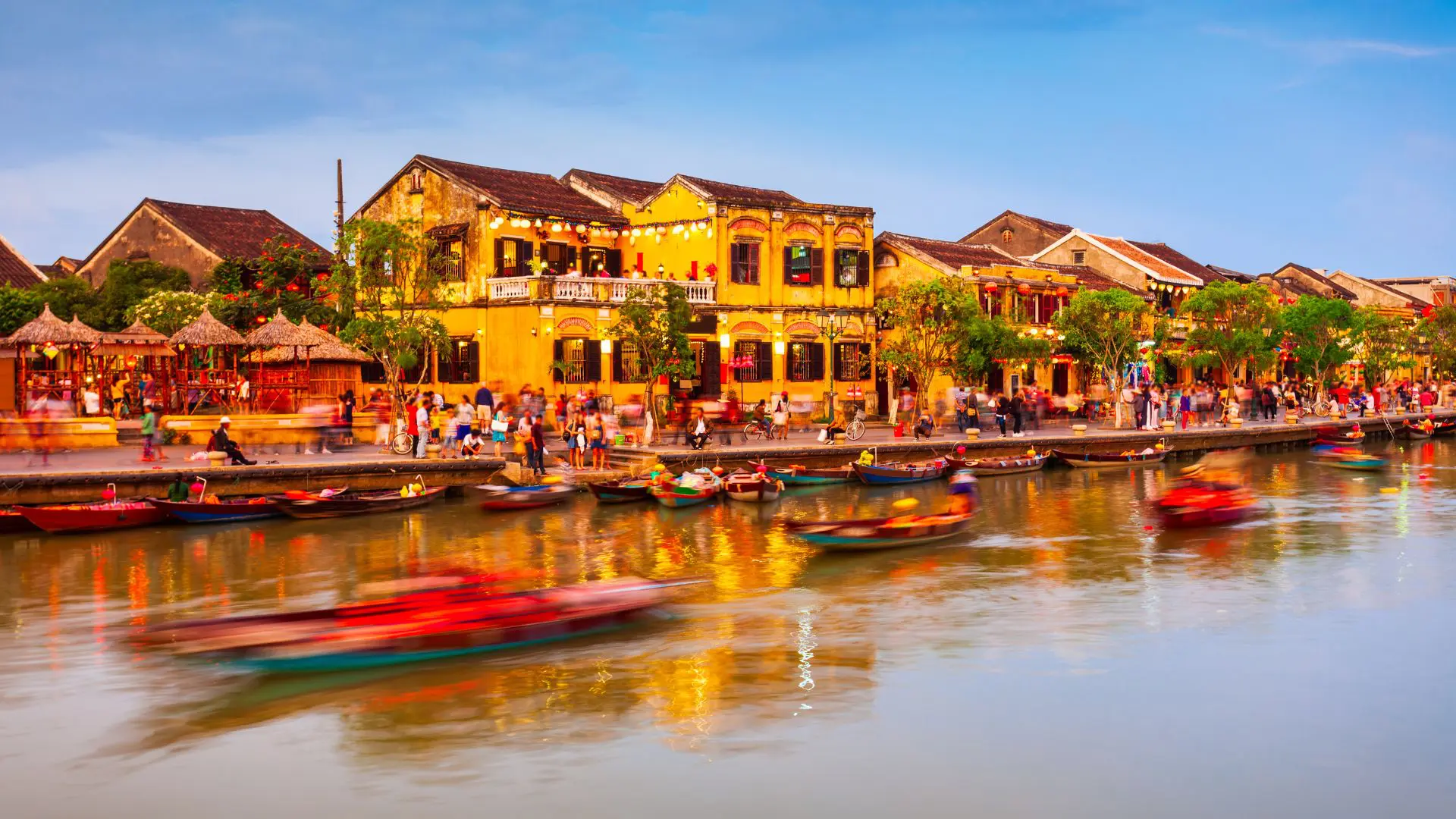 MERCADO DE HOI AN NO VIETNAME 2 Casas amarelas à beira do rio de Hoi An ao entardecer, com barcos em movimento e gente a passear