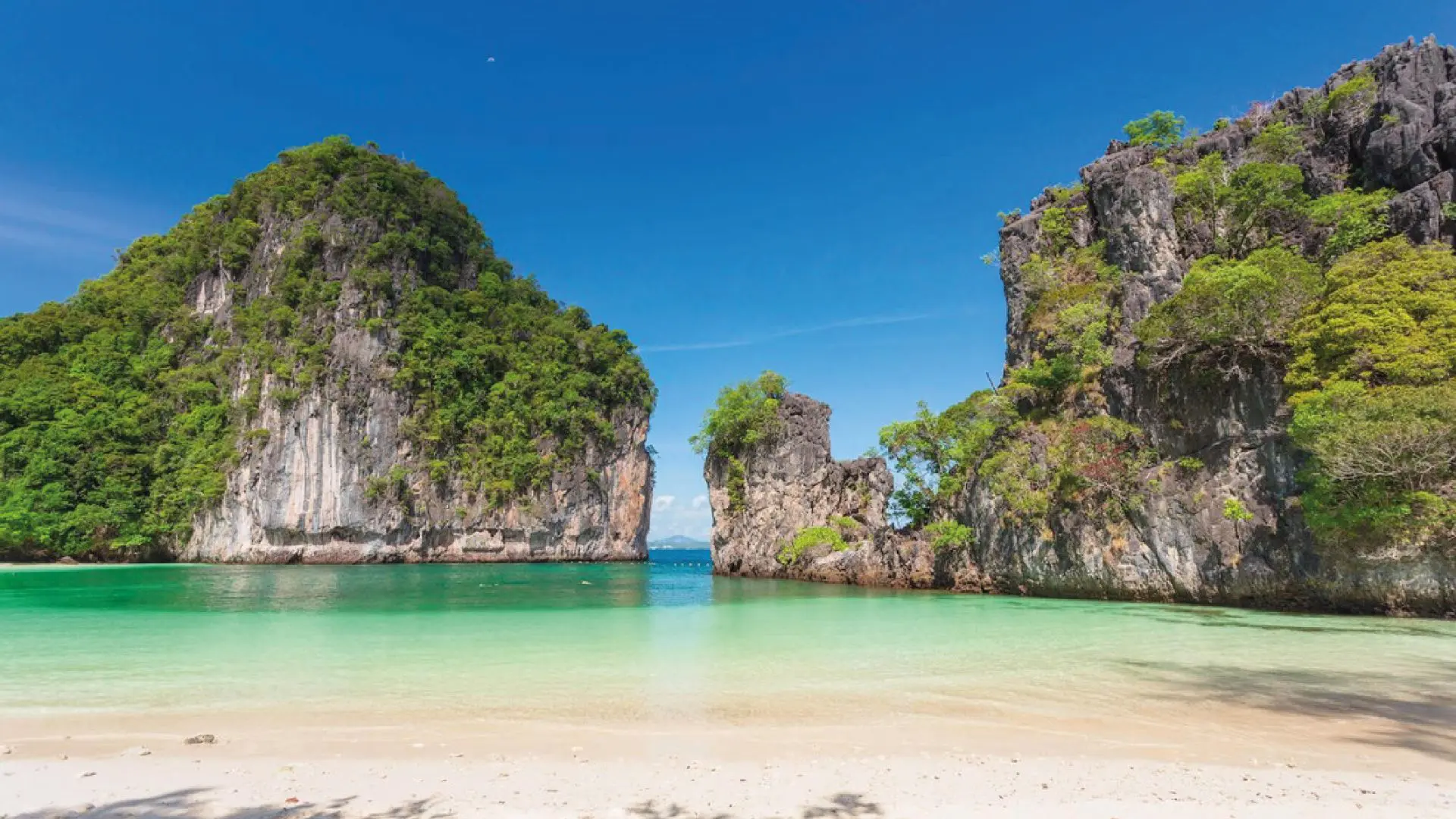 Deserted light-sand beach with emerald-green water between two large limestone sea stacks