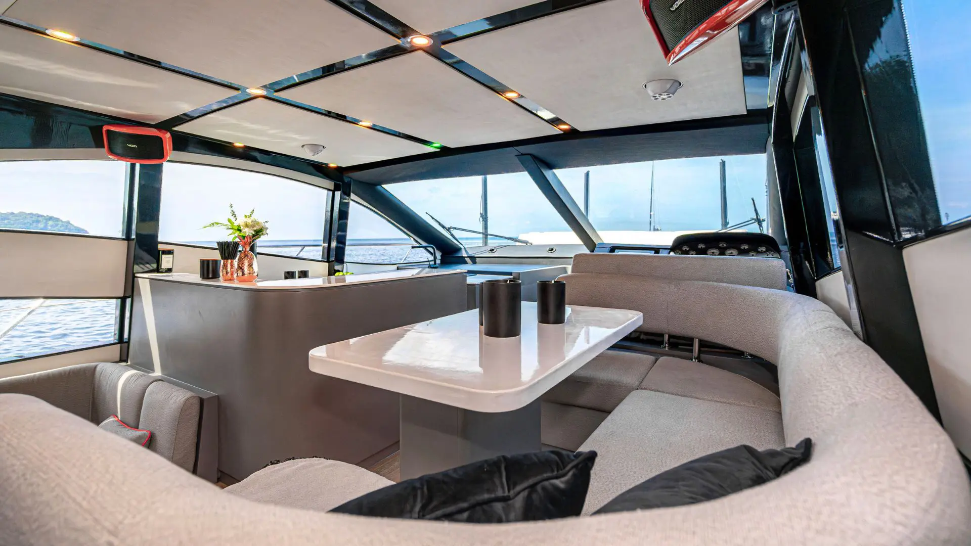 Sofá en U y mesa blanca en el salón de un yate, con barra, flores y vistas al mar por los ventanales