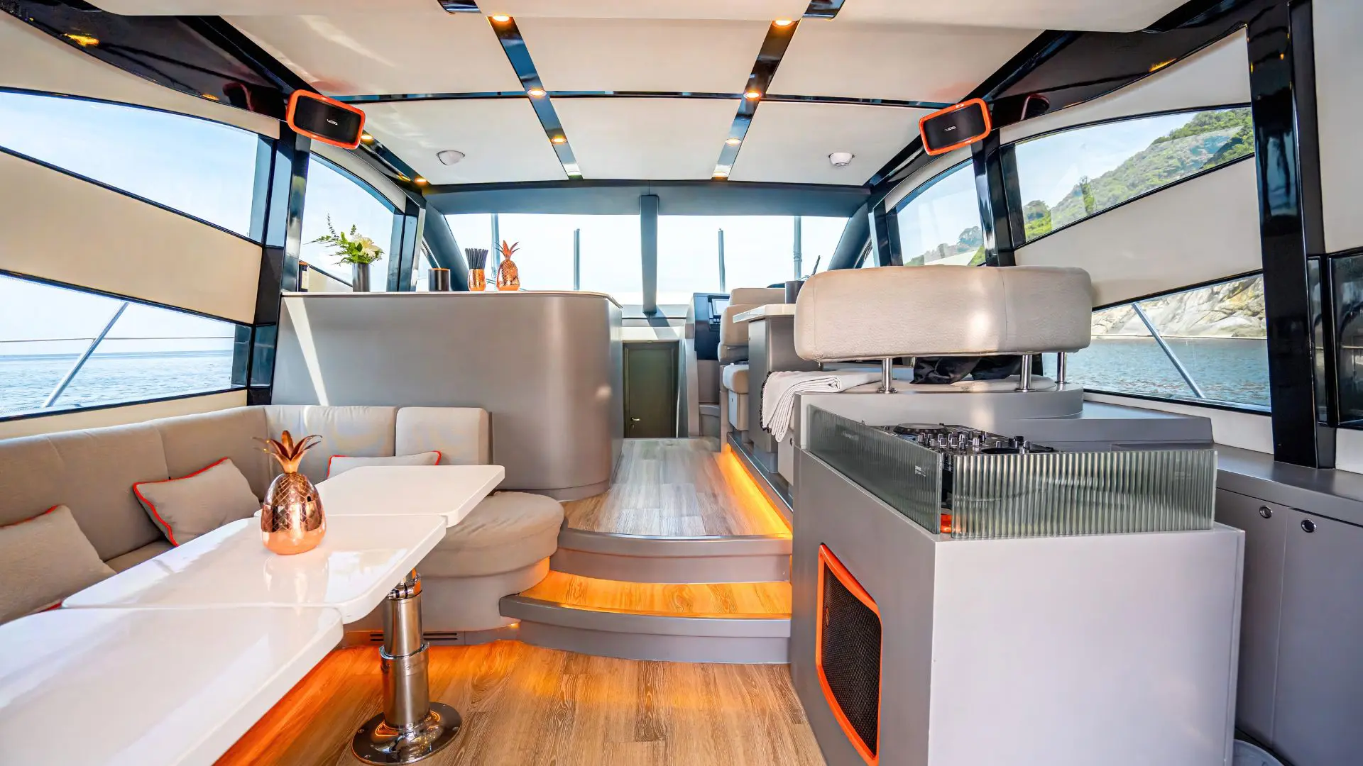 Salón interior de un yate con sofás, barra y una cabina de DJ con mesa de mezclas junto a los ventanales