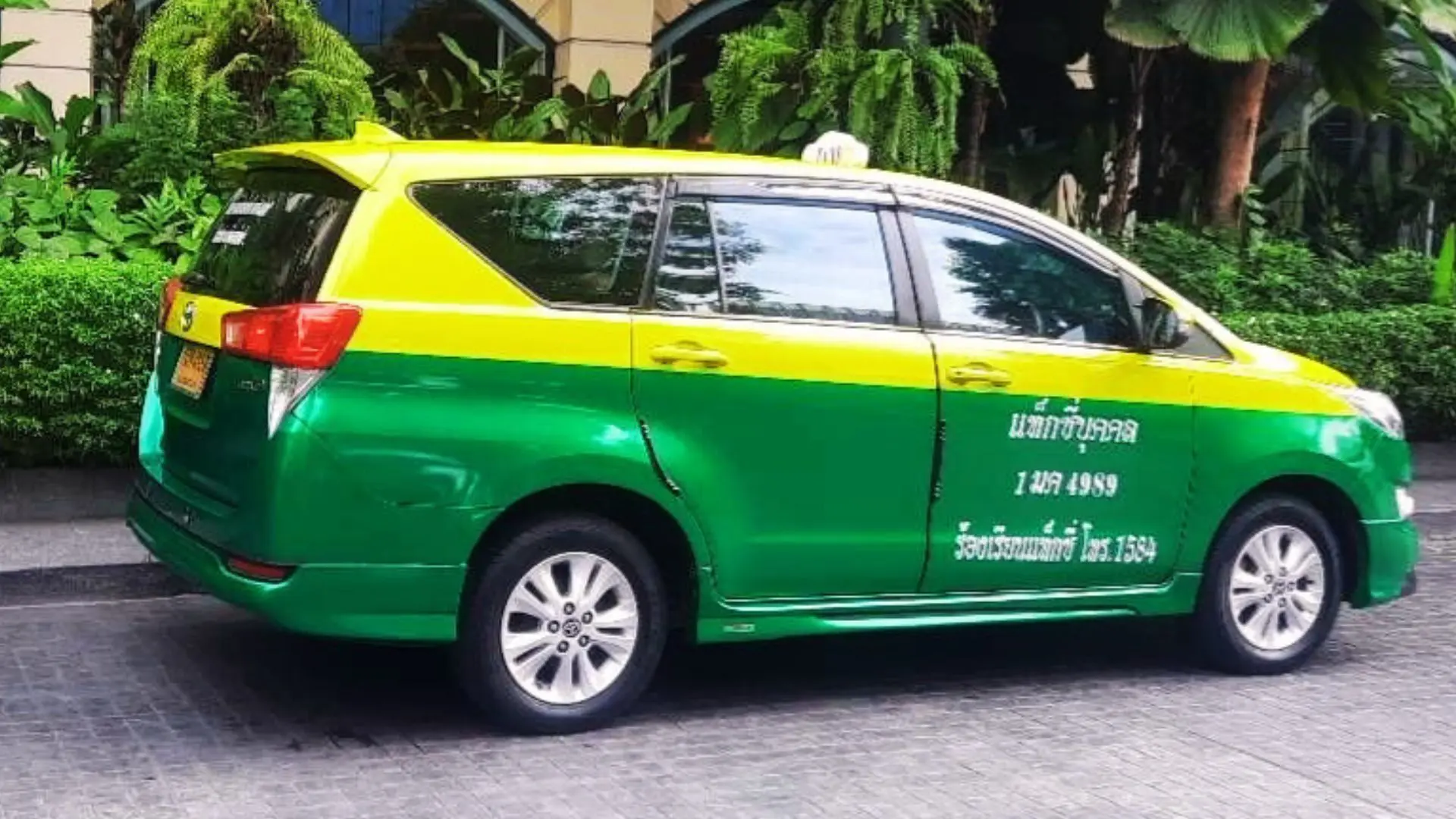 Táxi monovolume verde e amarelo estacionado junto a uma sebe e palmeiras