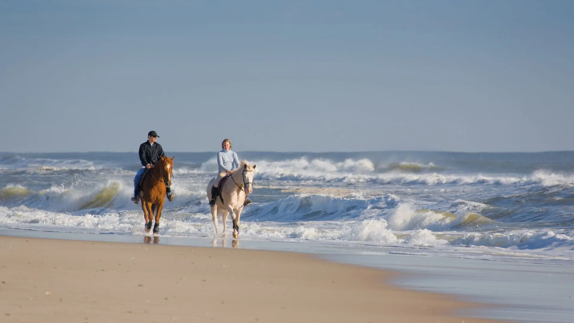 Andar a cavalo na praia em Phuket 8 Um homem num cavalo castanho e uma mulher num cavalo branco cavalgam pela beira-mar entre ondas de espuma branca
