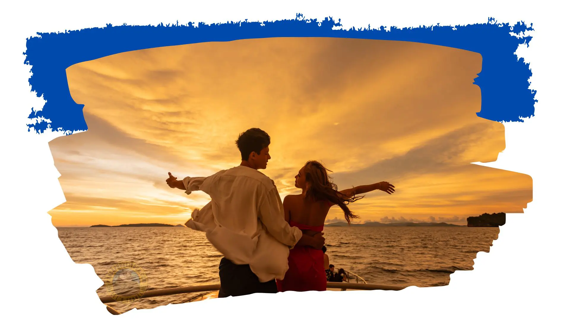 Um casal abre os braços no convés de um barco, em contraluz sob um céu dourado de pôr do sol sobre o mar