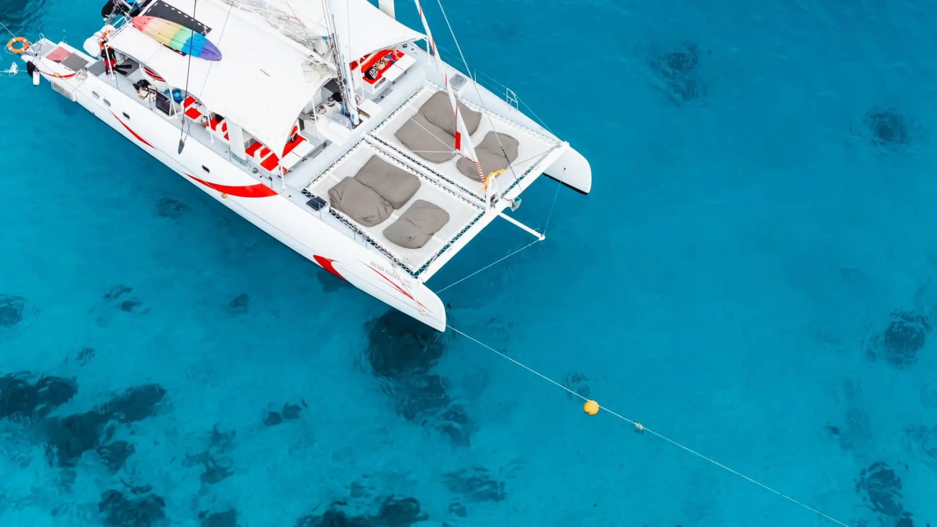 Catamaran deck seen from above: beige mats on the net and a colorful board tied down