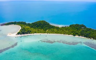 Ilha arborizada vista do ar, com uma longa praia branca e águas turquesa