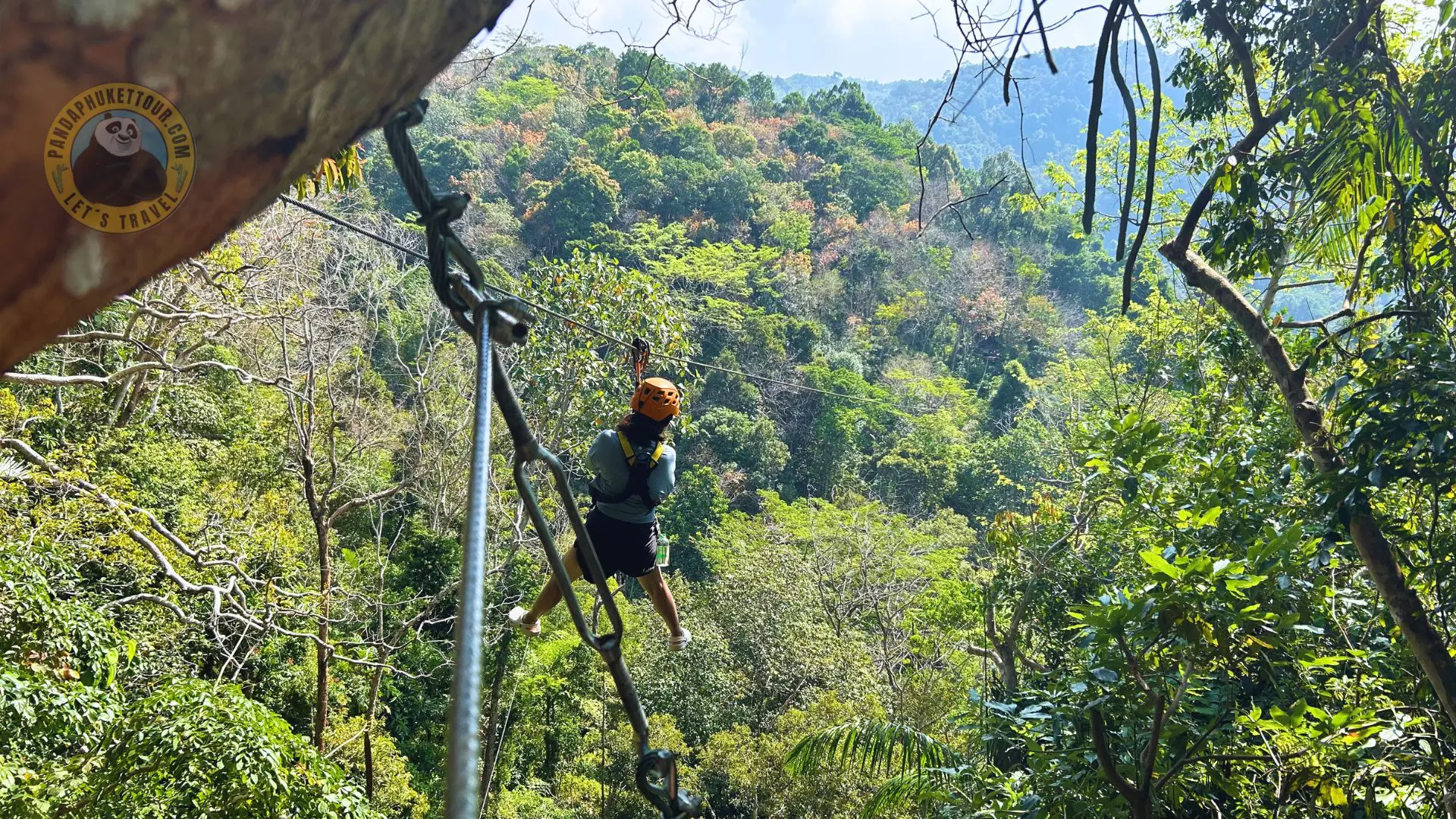 The Best Zipline in Phuket (11) A person in an orange helmet and harness rides the zip line over the jungle from a platform among trees