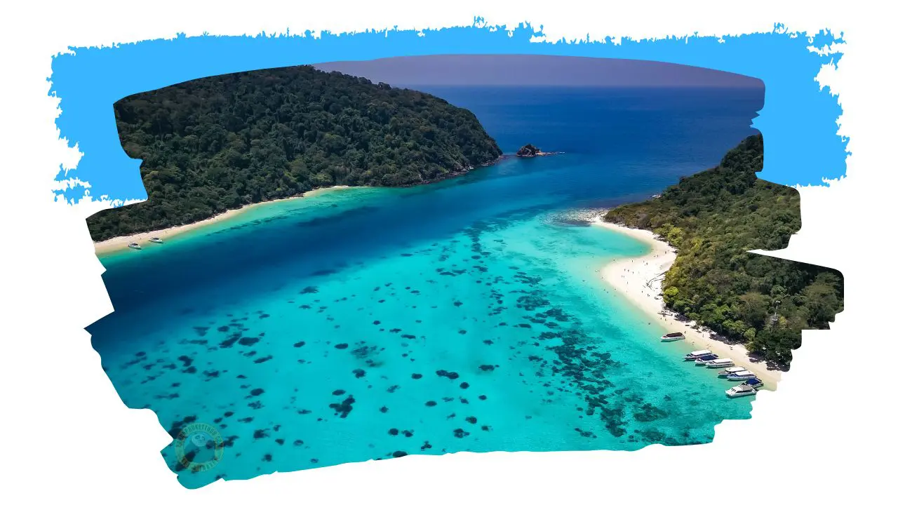Vista aérea de Koh Rok: duas ilhas de selva separadas por um canal turquesa com corais, numa moldura de pincelada azul