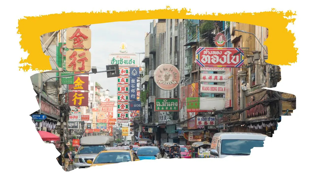 Rua de Chinatown repleta de letreiros chineses e tailandeses, com táxis e carrinhas no trânsito
